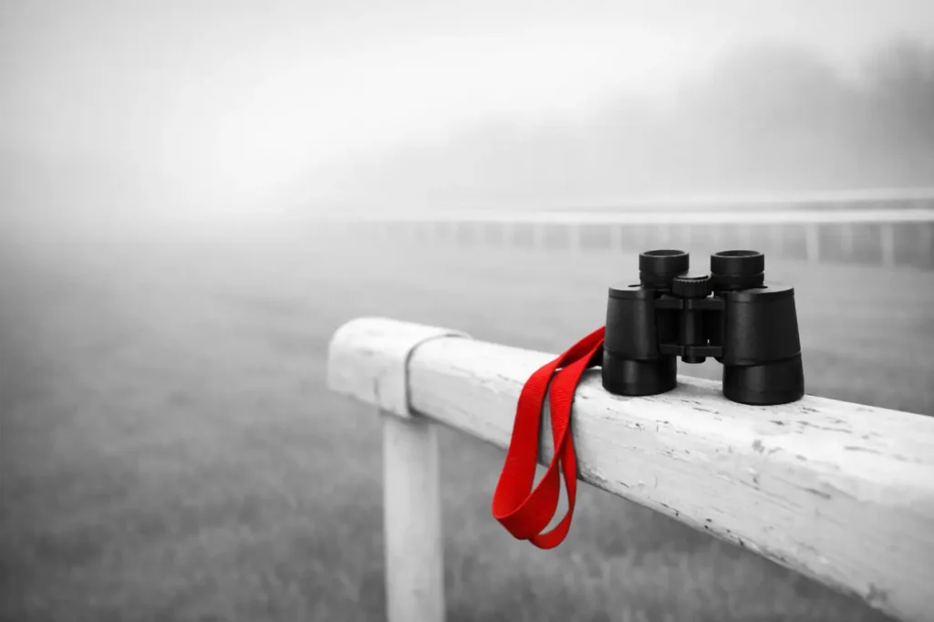 Best odds guaranteed: binoculars with a red strap resting on a misty racecourse rail